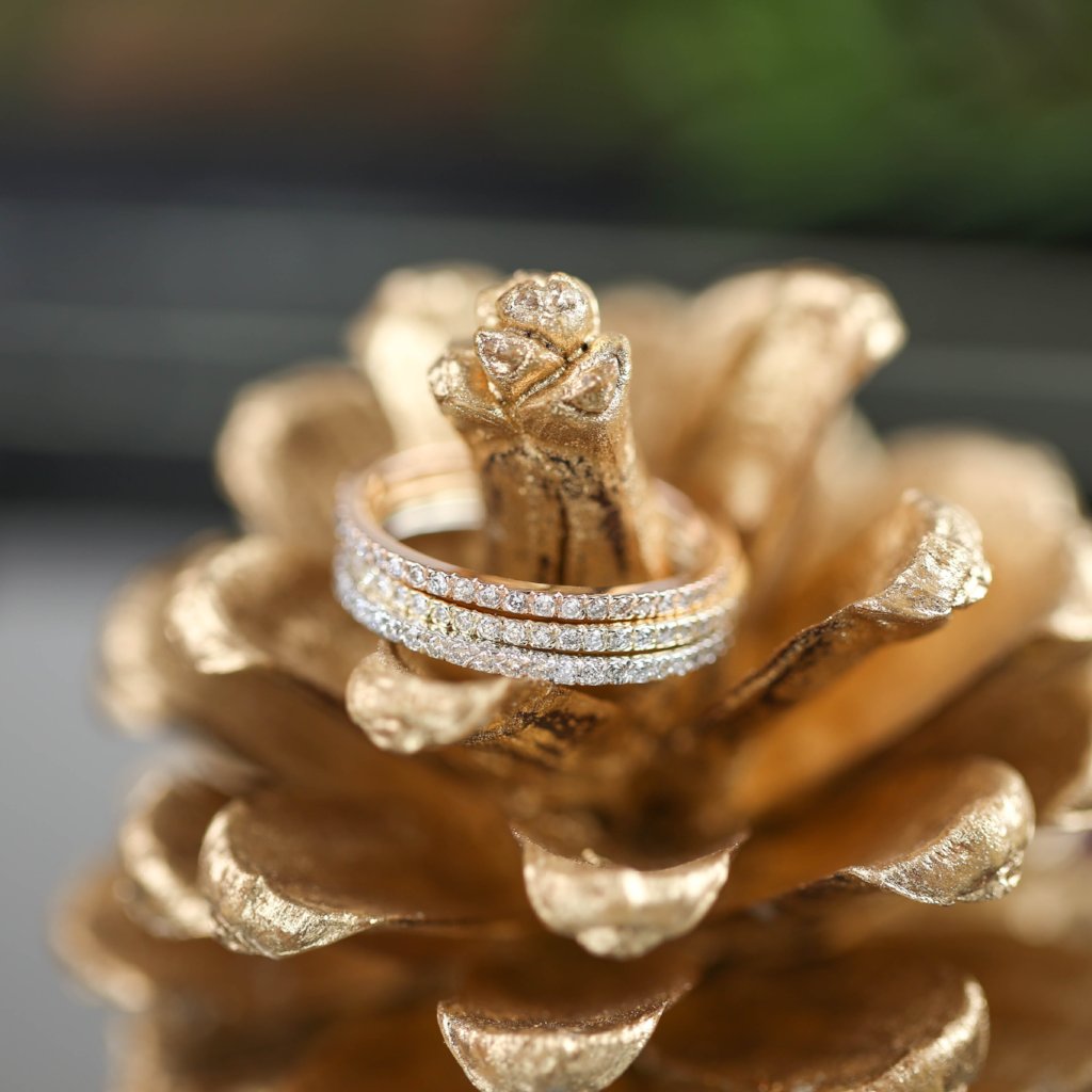 Close-up of Meteor Diamond Band 1.3mm with natural white diamonds on a gold-painted pinecone background