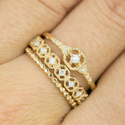 Close-up of a hand wearing three gold rings with milgrain detailing and small white diamonds