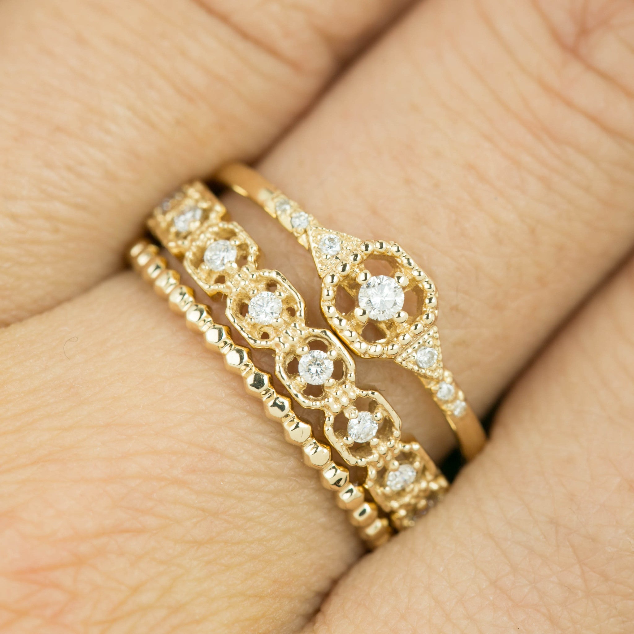 Close-up of a hand wearing three gold rings with milgrain detailing and small white diamonds