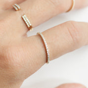 Thin 1.3mm natural white diamond band ring on finger in solid gold with recyclable kraft ring box packaging.