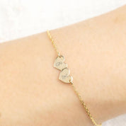 Delicate gold chain bracelet with two small heart-shaped engraved charms on a wrist close-up view.
