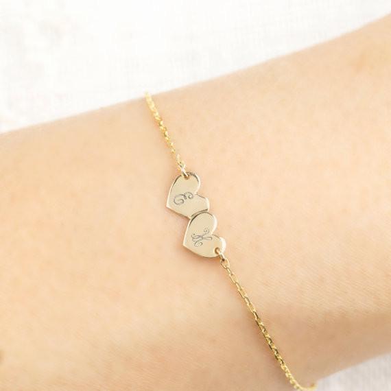 Delicate gold chain bracelet with two small heart-shaped engraved charms on a wrist close-up view.