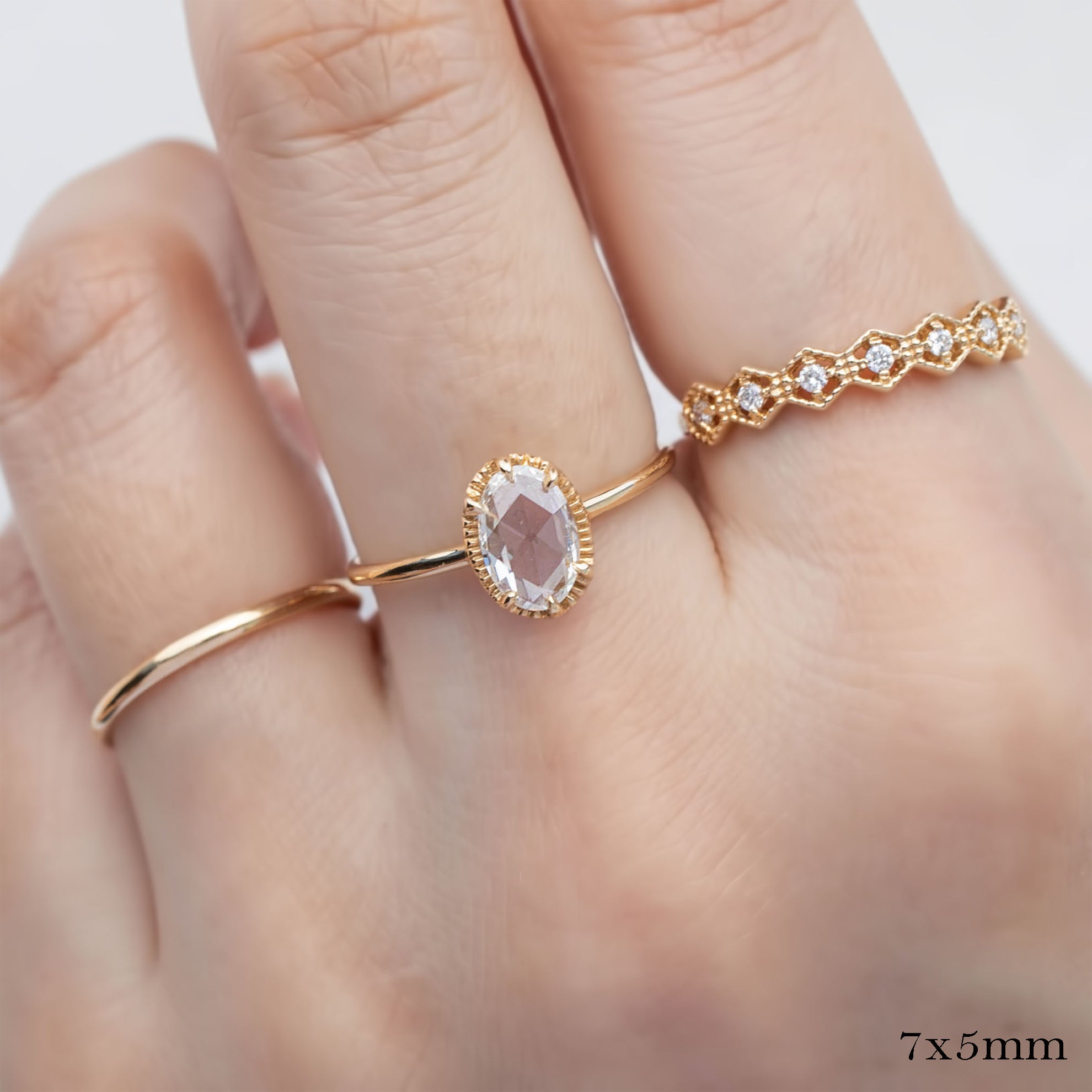 Close-up of hand wearing Ava Ring with oval rose cut diamond set in a delicate gold band with decorative bezel setting