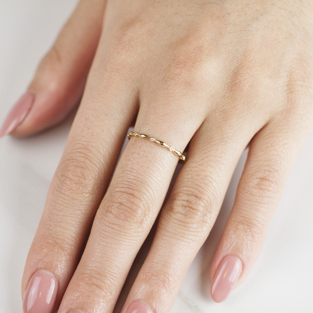 Close-up of a hand wearing a delicate Aria Eternity Ring with small white diamonds set in solid gold band
