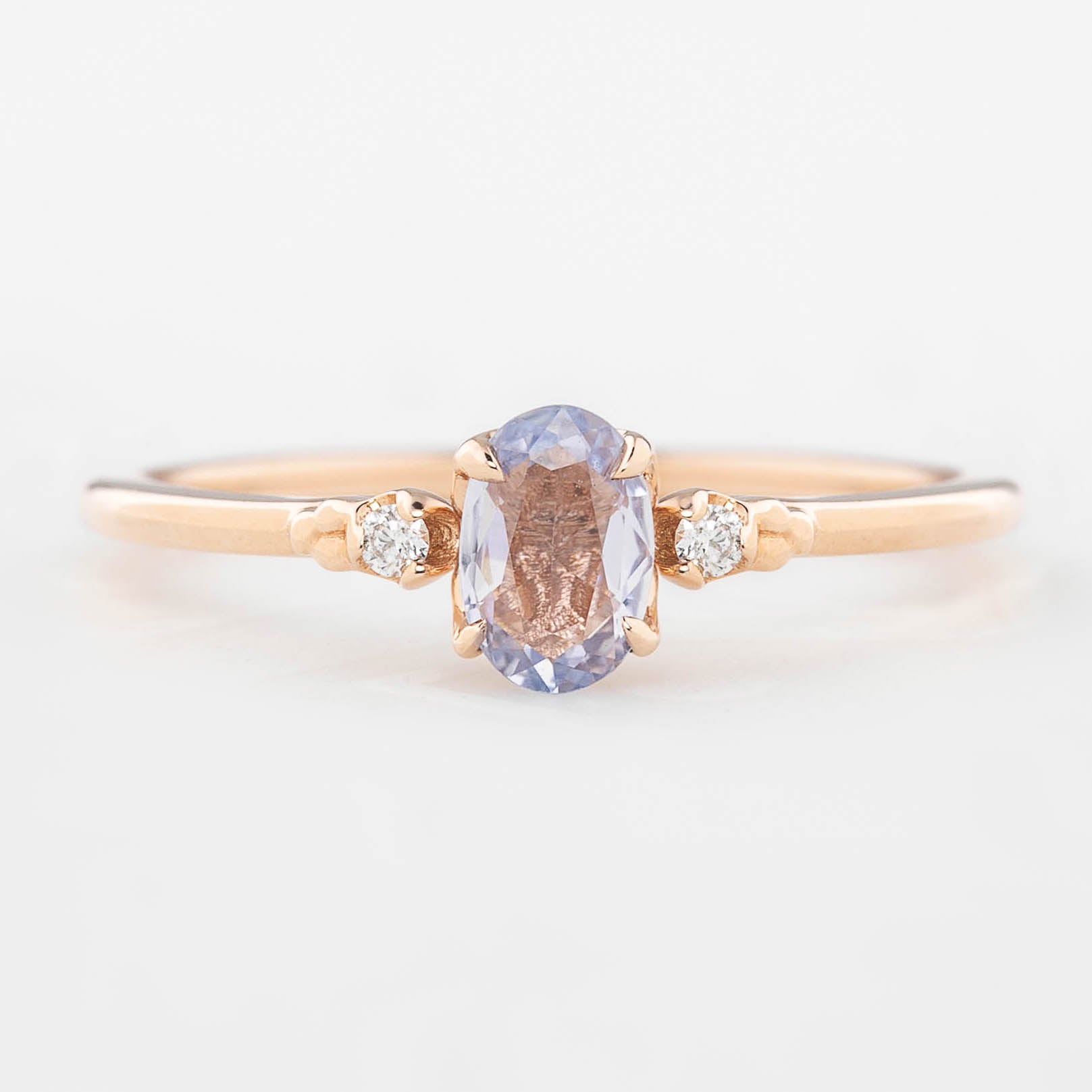 Three 'Estel Rings' with oval-shaped sapphires, in settings of 14k rose gold, 14k white gold, and 14k yellow gold, displayed against a light background., oval shape gemstone