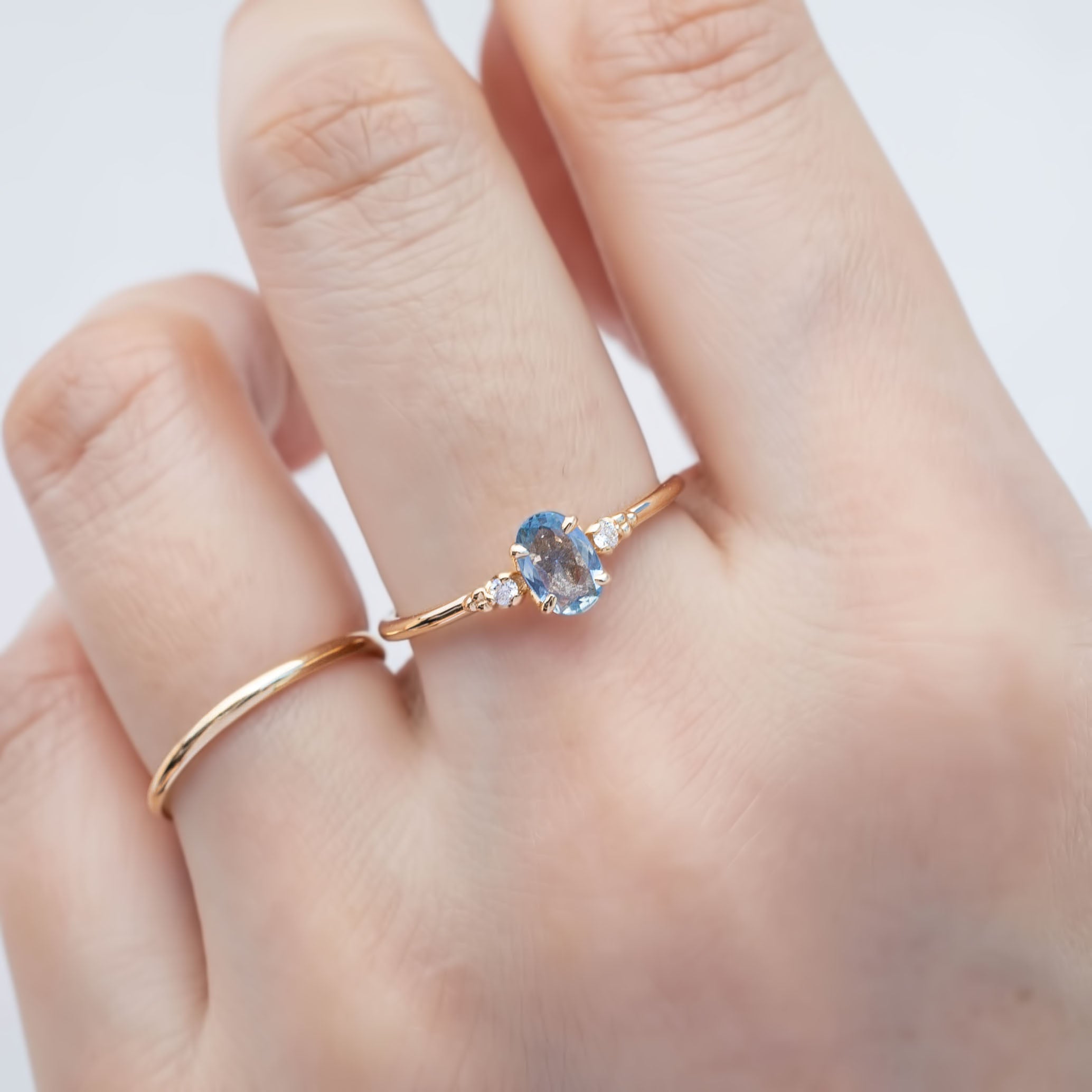 Three 'Estel Rings' with oval-shaped sapphires, in settings of 14k rose gold, 14k white gold, and 14k yellow gold, displayed against a light background., oval shape gemstone