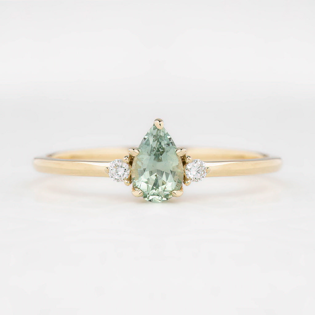 A pear-cut Montana sapphire ring with accent diamonds set in a 14k yellow gold band, displayed against a white background.