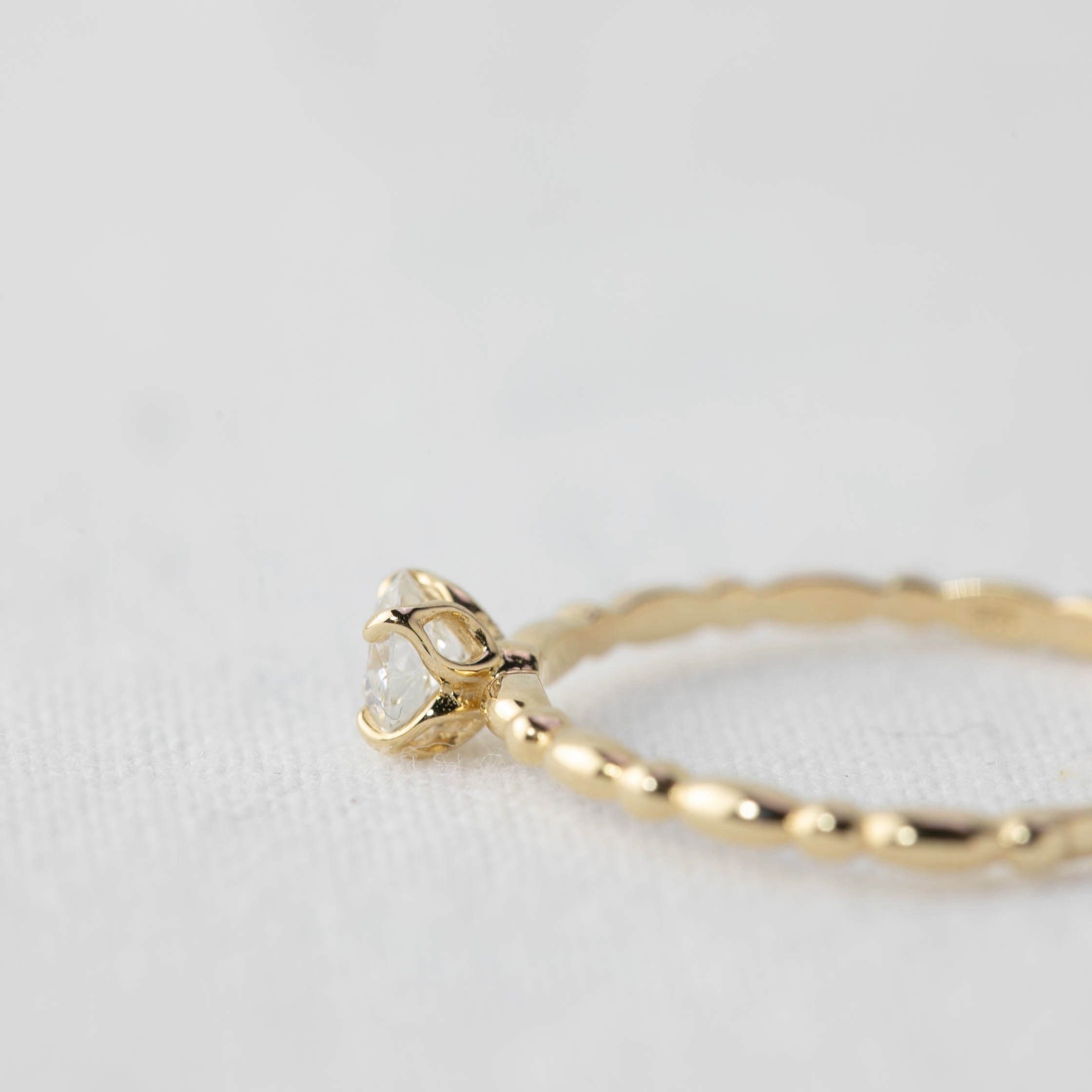 Close-up of a 0.25ct round brilliant cut diamond ring in 14k yellow gold with a flower prong setting on a white surface.