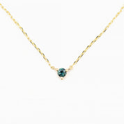 A gold-colored necklace with a round 3-4mm blue gemstone set in a three-prong setting with a spring ring clasp closure.