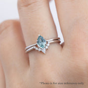Hand wearing a silver ring with a pear-shaped blue sapphire and small diamonds in a delicate setting.