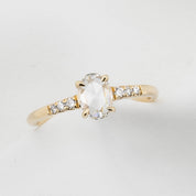 Gold ring with a central gemstone and smaller diamonds on a light gray background