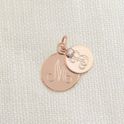 Two rose gold engraved circle pendants with a small gemstone on a textured fabric background