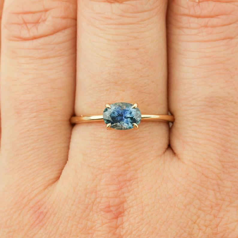 Sara Ring featuring a 1ct parti blue green Montana Sapphire set in recycled 14k yellow gold band, size 7 shown on finger