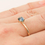 Close-up of a 1.00ct blue green Montana sapphire ring set in recycled 14k yellow gold on a hand.