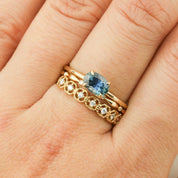 Close-up of a hand wearing a 14k yellow gold Sara Ring with a 1ct blue green Montana sapphire and diamond band