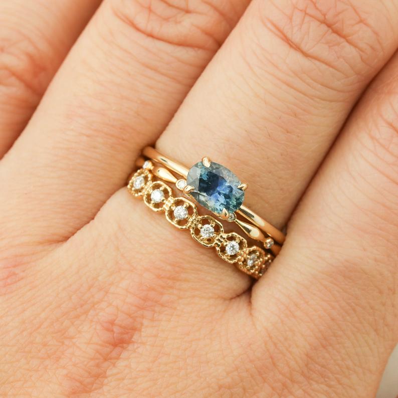 Close-up of a hand wearing a 14k yellow gold Sara Ring with a 1ct blue green Montana sapphire and diamond band
