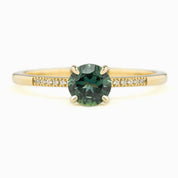 Audrey Ring with a 0.73ct Teal Blue Queensland Sapphire center stone, set in a 14K Yellow Gold band with small diamond accents.