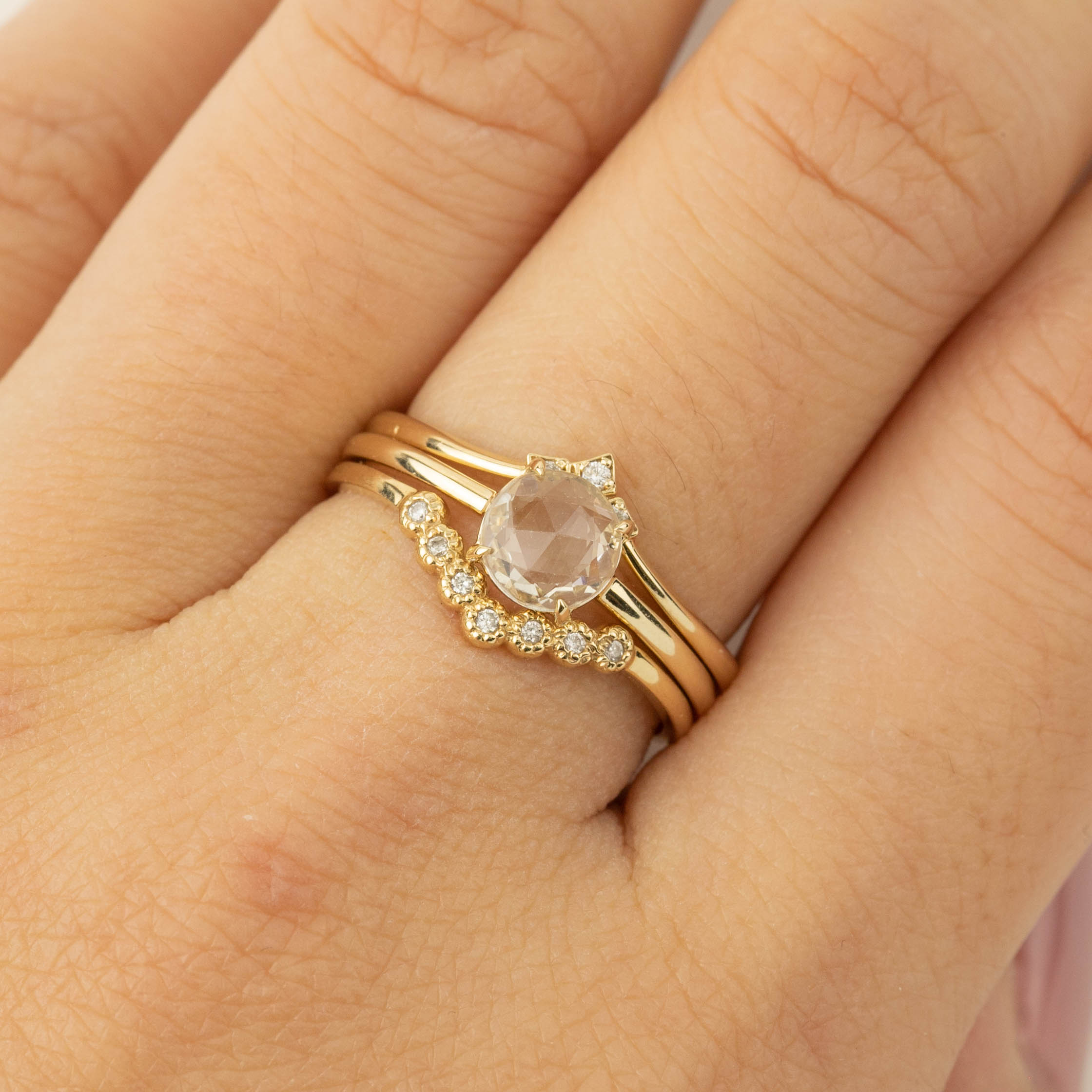 Close-up of a hand wearing a 0.88ct white sapphire Lisa Ring set in recycled 14k gold with small accent diamonds.