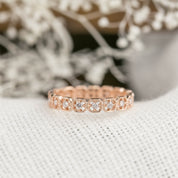 Rose gold milgrain square eternity ring with natural white diamonds set in a detailed band on neutral fabric background.