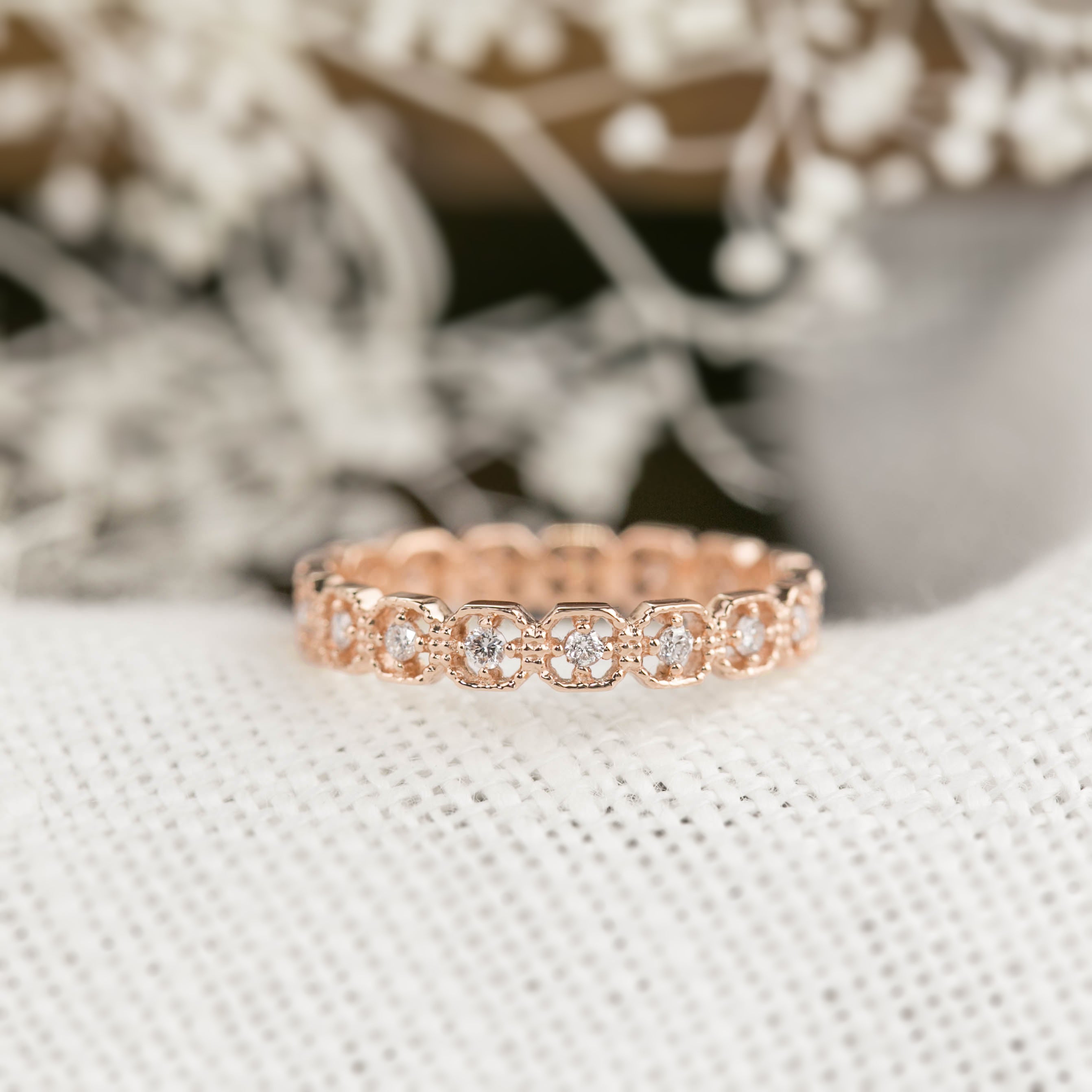 Rose gold milgrain square eternity ring with natural white diamonds set in a detailed band on neutral fabric background.