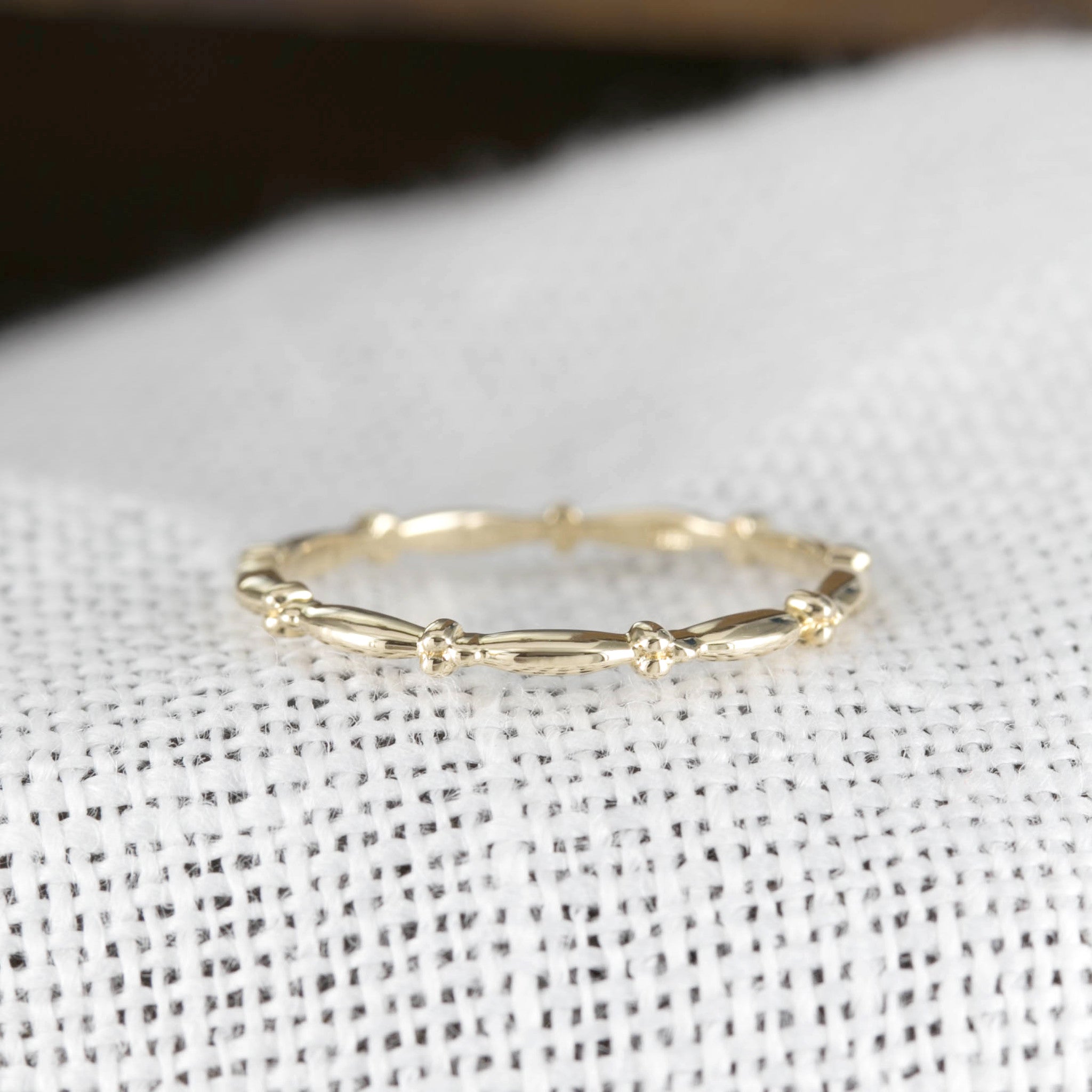 Ethically sourced solid gold Julia Ring with full eternity bead design and 1.7mm band width on textured fabric background
