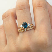 Hand wearing three gold rings including a gold band with diamonds and a ring with a large dark blue gemstone centerpiece
