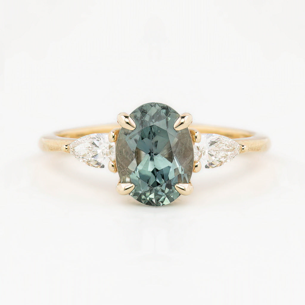 An oval-cut Montana Sapphire ring with color-changing light blue-green to purple, flanked by two accent diamonds, set in solid 14k yellow gold.