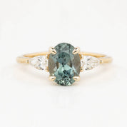 An oval-cut Montana Sapphire ring with color-changing light blue-green to purple, flanked by two accent diamonds, set in solid 14k yellow gold.