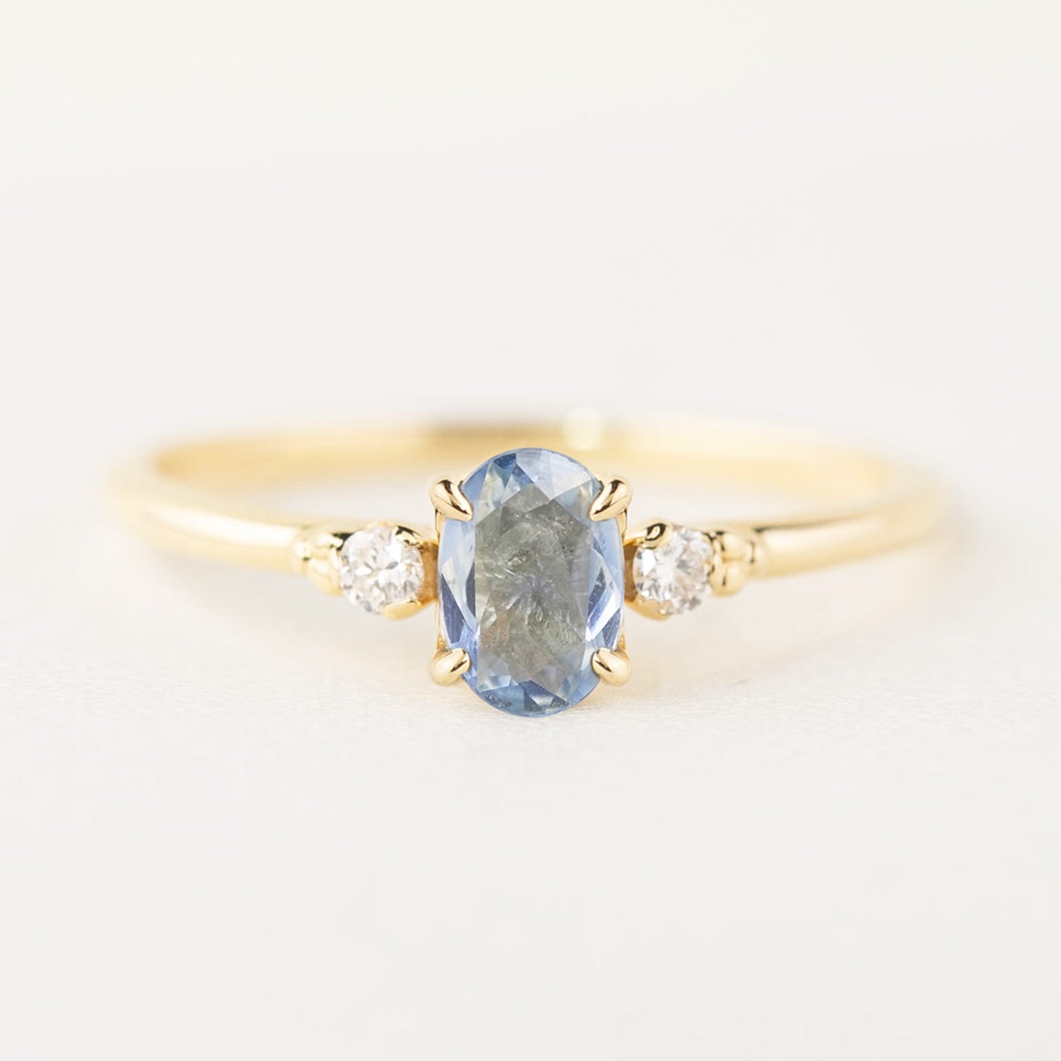 Three 'Estel Rings' with oval-shaped sapphires, in settings of 14k rose gold, 14k white gold, and 14k yellow gold, displayed against a light background., oval shape gemstone