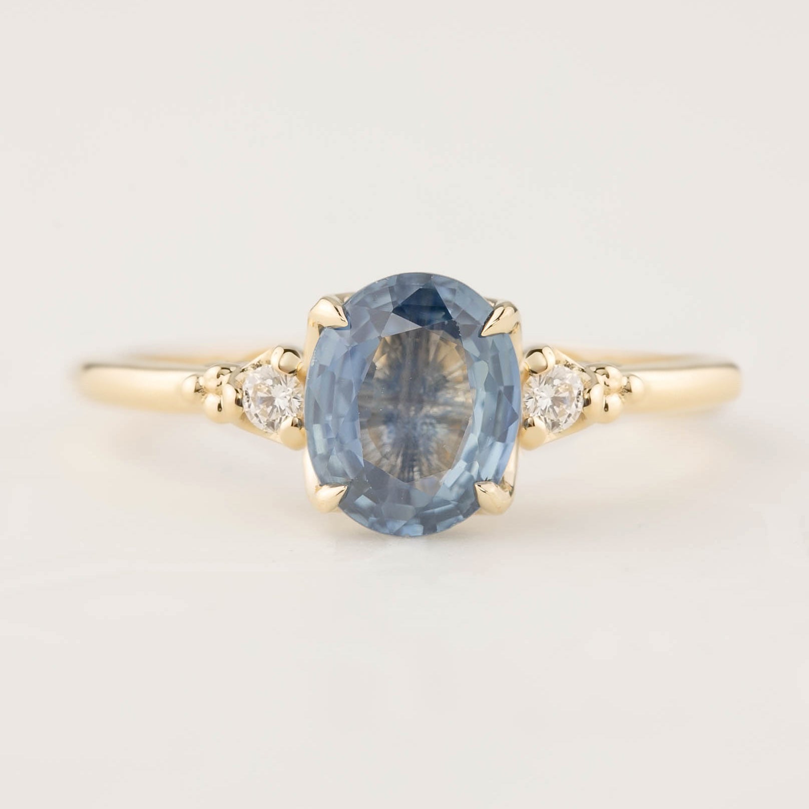 Gold ring featuring a 1.53ct oval blue sapphire and two small white diamond accents in a four-prong setting