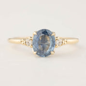 Gold ring featuring a 1.53ct oval blue sapphire and two small white diamond accents in a four-prong setting