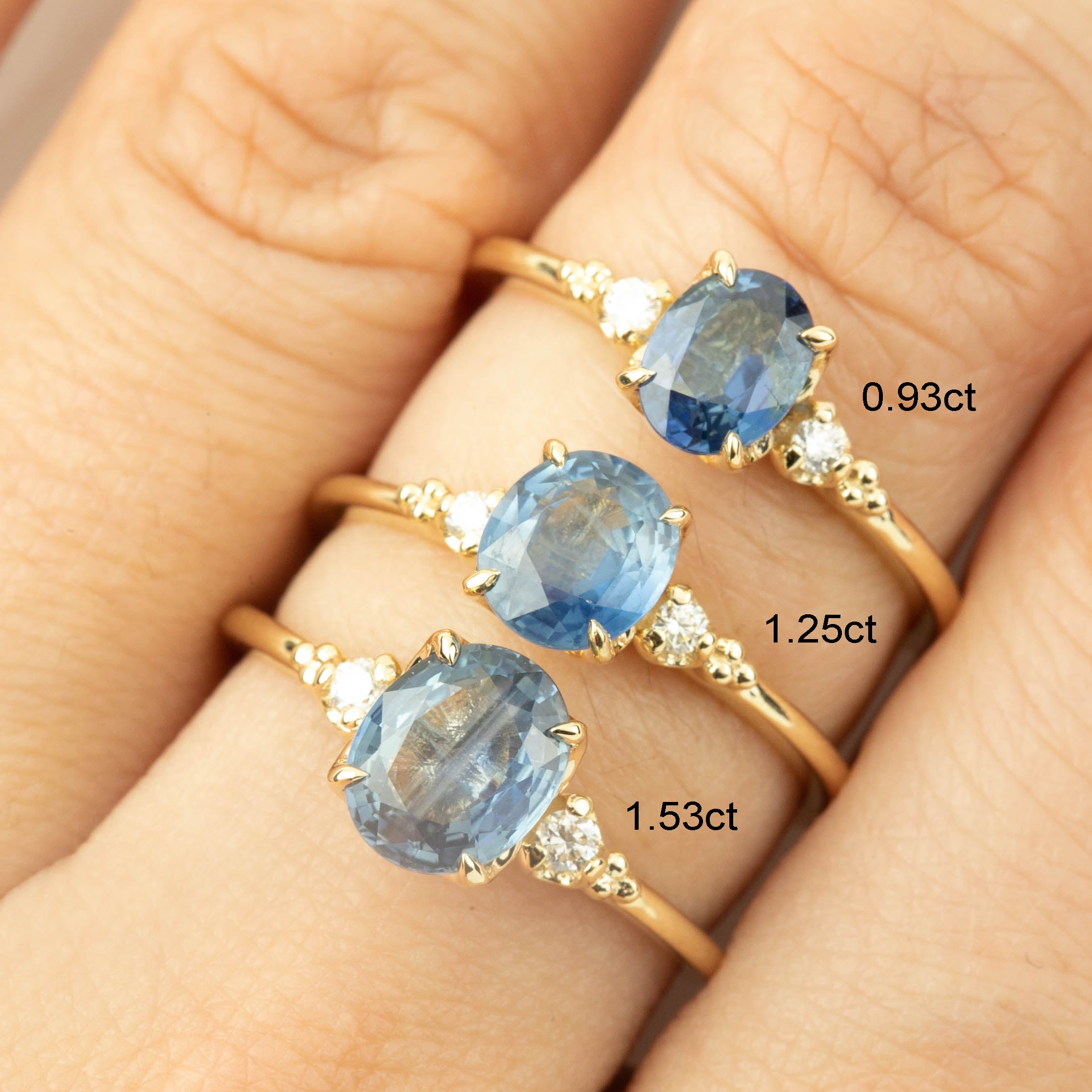Close-up of three 14k gold rings with blue sapphires and small accent diamonds on a hand.